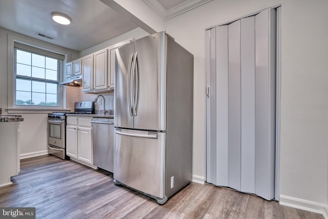 kitchen with light hardwood / wood-style flooring, ornamental molding, appliances with stainless steel finishes, tasteful backsplash, and white cabinetry