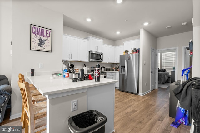 kitchen featuring white cabinets, a kitchen breakfast bar, light hardwood / wood-style flooring, appliances with stainless steel finishes, and kitchen peninsula