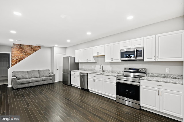 kitchen with light stone counters, stainless steel appliances, dark wood-type flooring, sink, and white cabinets