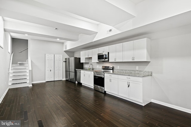 kitchen with white cabinets, dark hardwood / wood-style floors, light stone counters, and stainless steel appliances