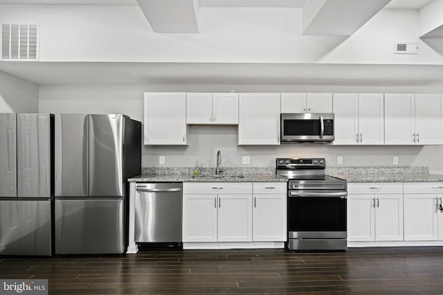 kitchen with light stone countertops, white cabinetry, sink, stainless steel appliances, and dark hardwood / wood-style flooring