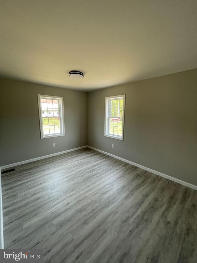 spare room with wood finished floors, visible vents, and baseboards