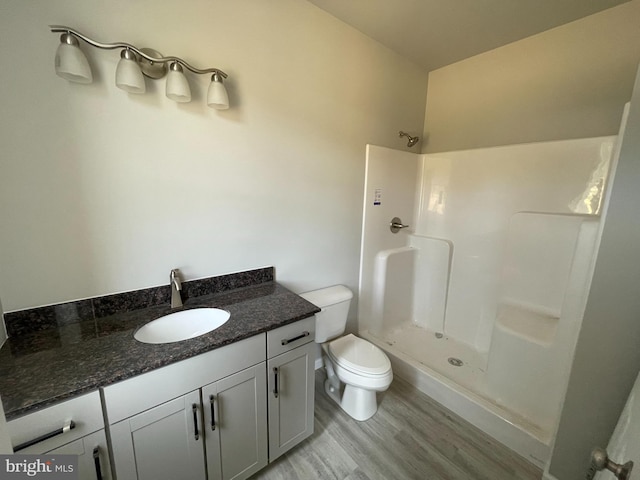 full bathroom featuring toilet, a shower, wood finished floors, and vanity