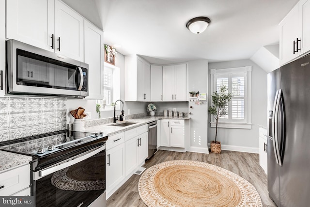 kitchen featuring light stone countertops, stainless steel appliances, sink, white cabinets, and light hardwood / wood-style floors