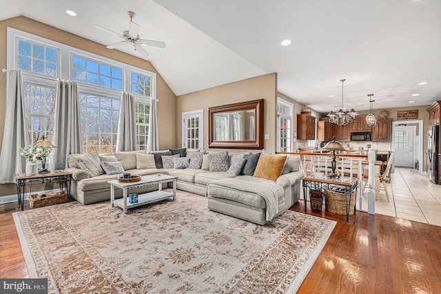 living room with vaulted ceiling, light hardwood / wood-style flooring, and ceiling fan with notable chandelier