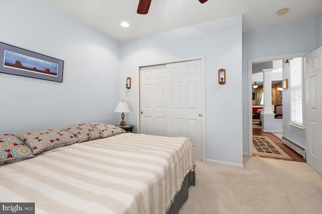 carpeted bedroom with ceiling fan, decorative columns, a baseboard radiator, and a closet