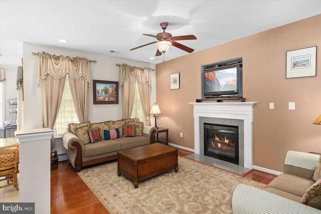 living room featuring baseboard heating, ceiling fan, a healthy amount of sunlight, and hardwood / wood-style flooring