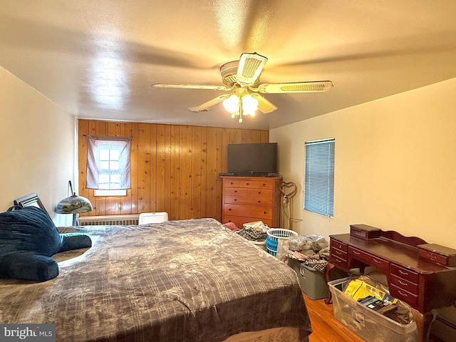 bedroom with ceiling fan, wooden walls, and wood-type flooring