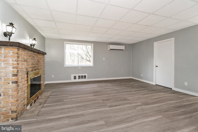 unfurnished living room with a wall mounted air conditioner, a paneled ceiling, wood-type flooring, and a fireplace