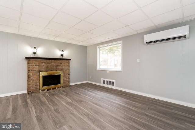 unfurnished living room with a fireplace, hardwood / wood-style floors, an AC wall unit, and a drop ceiling