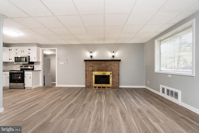 unfurnished living room featuring a fireplace, light hardwood / wood-style flooring, and a drop ceiling