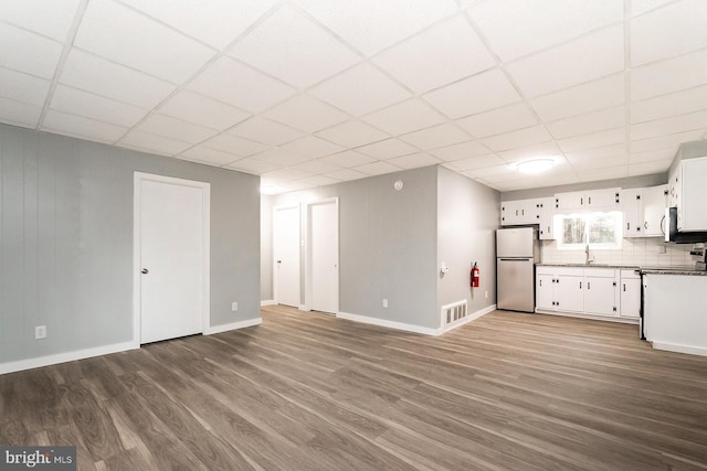 interior space featuring decorative backsplash, sink, hardwood / wood-style floors, white cabinetry, and stainless steel refrigerator