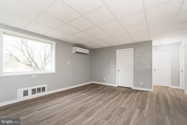 basement with hardwood / wood-style floors, a drop ceiling, and a wall mounted air conditioner