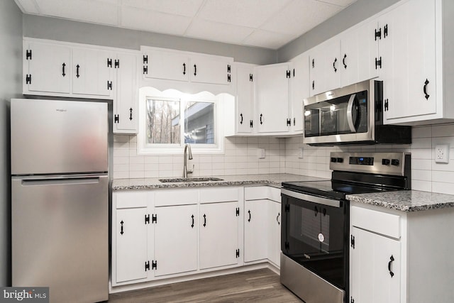 kitchen with dark hardwood / wood-style flooring, light stone counters, stainless steel appliances, sink, and white cabinets