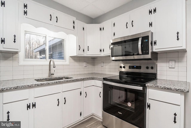 kitchen with light stone countertops, sink, stainless steel appliances, tasteful backsplash, and white cabinets