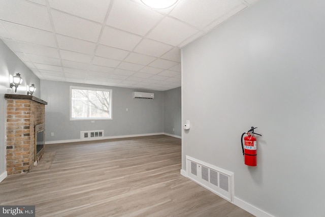 basement featuring a fireplace, a paneled ceiling, light hardwood / wood-style floors, and a wall unit AC