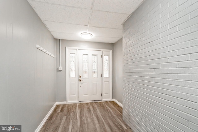 doorway to outside featuring a drop ceiling, brick wall, and hardwood / wood-style flooring