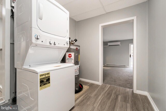 washroom with a baseboard radiator, water heater, a wall unit AC, stacked washer and clothes dryer, and hardwood / wood-style flooring