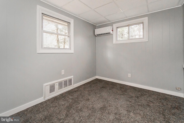 carpeted empty room with a wall unit AC and a drop ceiling