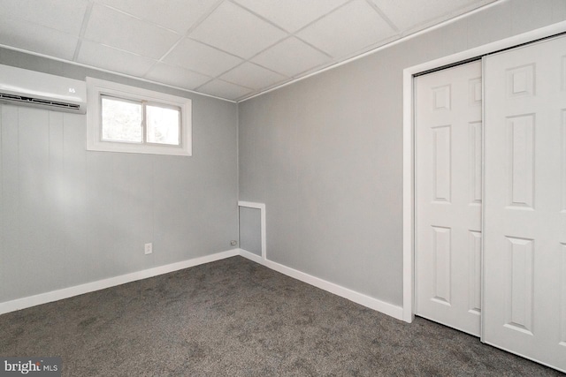 interior space with dark colored carpet, a paneled ceiling, an AC wall unit, and a closet