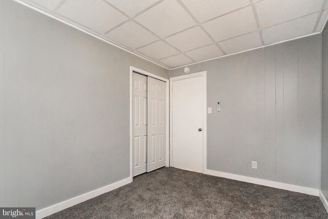 unfurnished bedroom with a closet, a drop ceiling, and dark colored carpet