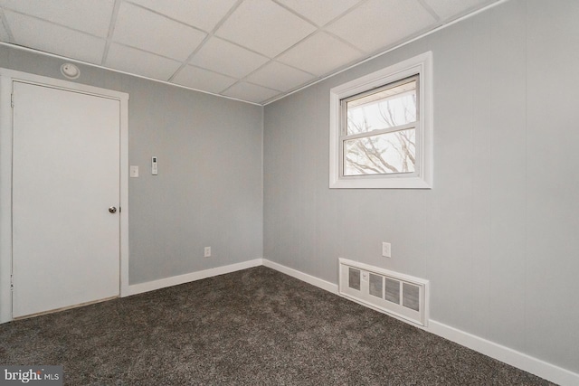 spare room with dark colored carpet and a paneled ceiling