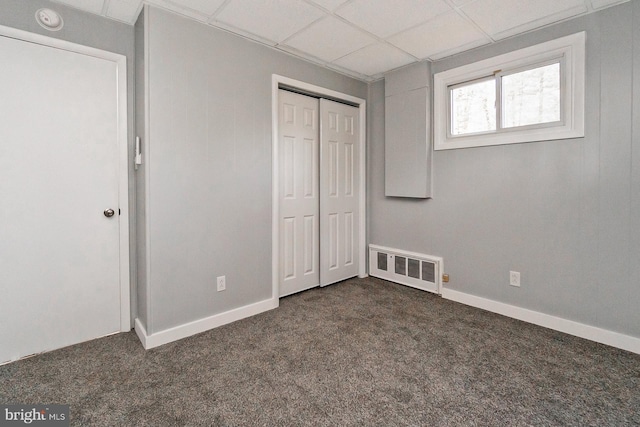 unfurnished bedroom with a drop ceiling, dark carpet, and a closet