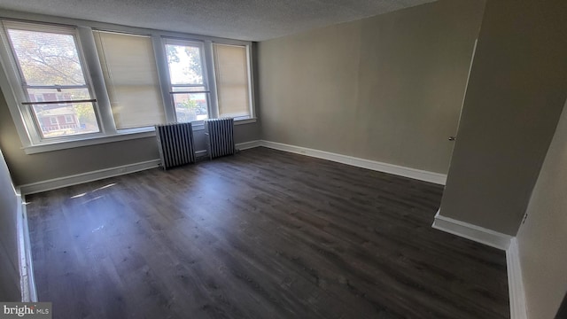 spare room featuring plenty of natural light, dark hardwood / wood-style floors, a textured ceiling, and radiator heating unit