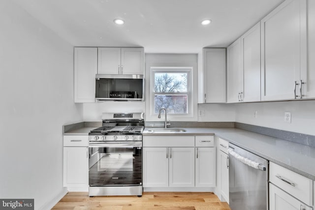 kitchen with white cabinets, sink, appliances with stainless steel finishes, and light hardwood / wood-style flooring