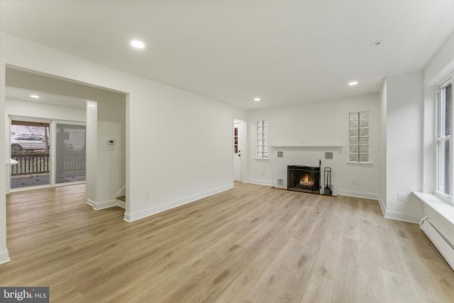 unfurnished living room featuring plenty of natural light, a baseboard radiator, and light hardwood / wood-style flooring