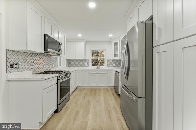 kitchen with white cabinetry, light stone countertops, tasteful backsplash, light hardwood / wood-style floors, and appliances with stainless steel finishes