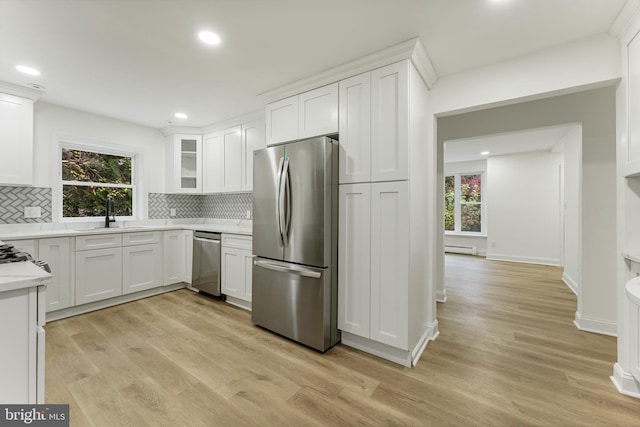 kitchen with white cabinets, backsplash, stainless steel appliances, and light hardwood / wood-style flooring