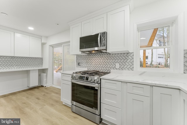 kitchen featuring appliances with stainless steel finishes, radiator, a healthy amount of sunlight, light hardwood / wood-style floors, and white cabinetry