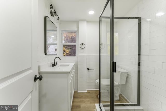 bathroom featuring vanity, a shower with door, wood-type flooring, tile walls, and toilet