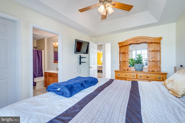 bedroom with a raised ceiling, connected bathroom, and ceiling fan