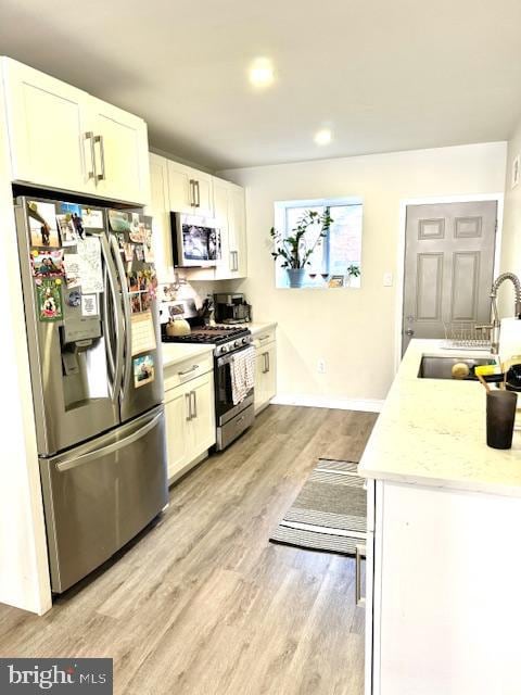 kitchen with a sink, stainless steel appliances, white cabinets, light wood finished floors, and light countertops