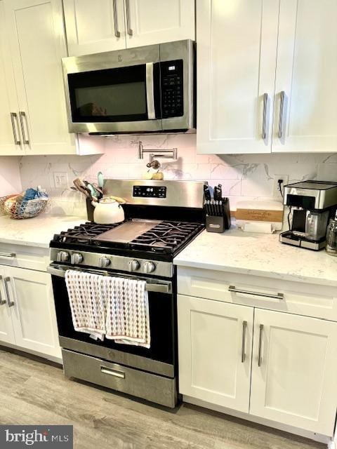 kitchen with light stone countertops, appliances with stainless steel finishes, light wood-type flooring, backsplash, and white cabinetry