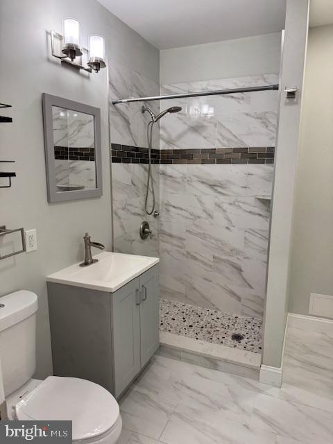 bathroom with tiled shower, vanity, and toilet