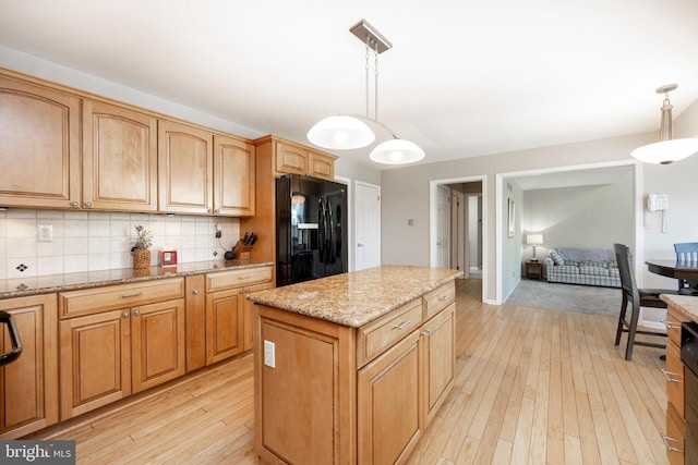 kitchen with decorative light fixtures, a center island, black fridge with ice dispenser, and light hardwood / wood-style flooring