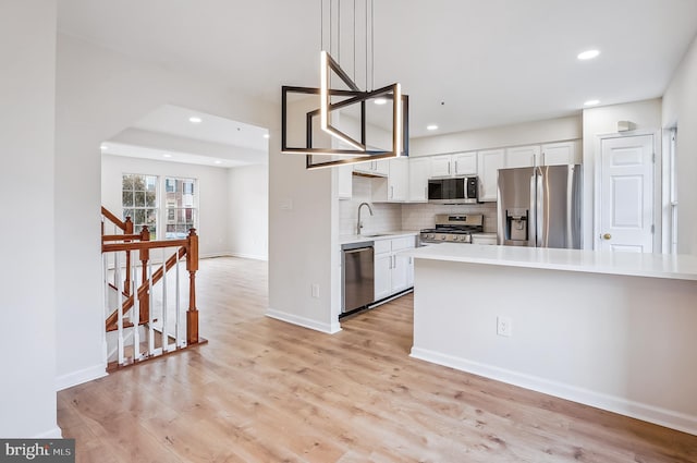 kitchen with white cabinets, appliances with stainless steel finishes, light hardwood / wood-style floors, and pendant lighting