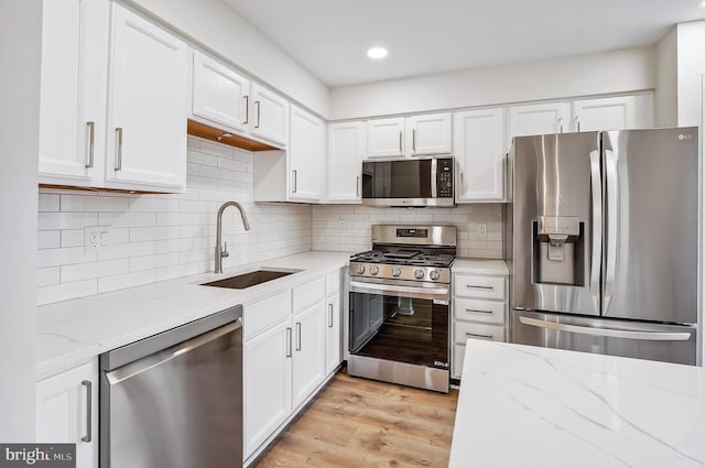 kitchen with appliances with stainless steel finishes, light hardwood / wood-style floors, white cabinetry, and sink