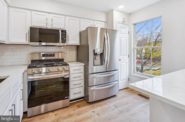 kitchen with plenty of natural light, white cabinets, light hardwood / wood-style flooring, and appliances with stainless steel finishes