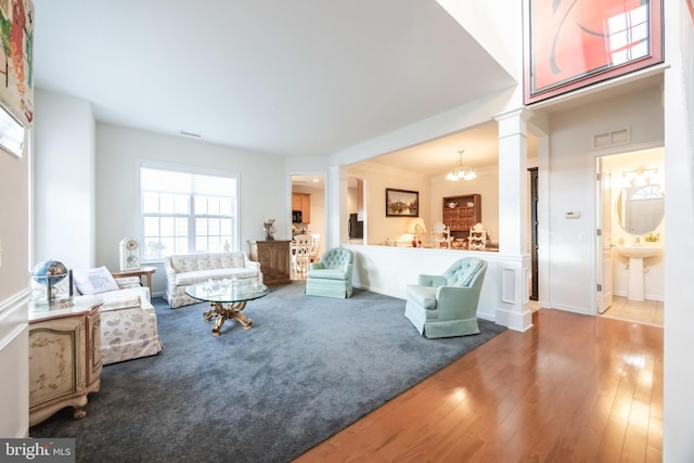 living room featuring ornate columns, wood-type flooring, and a notable chandelier