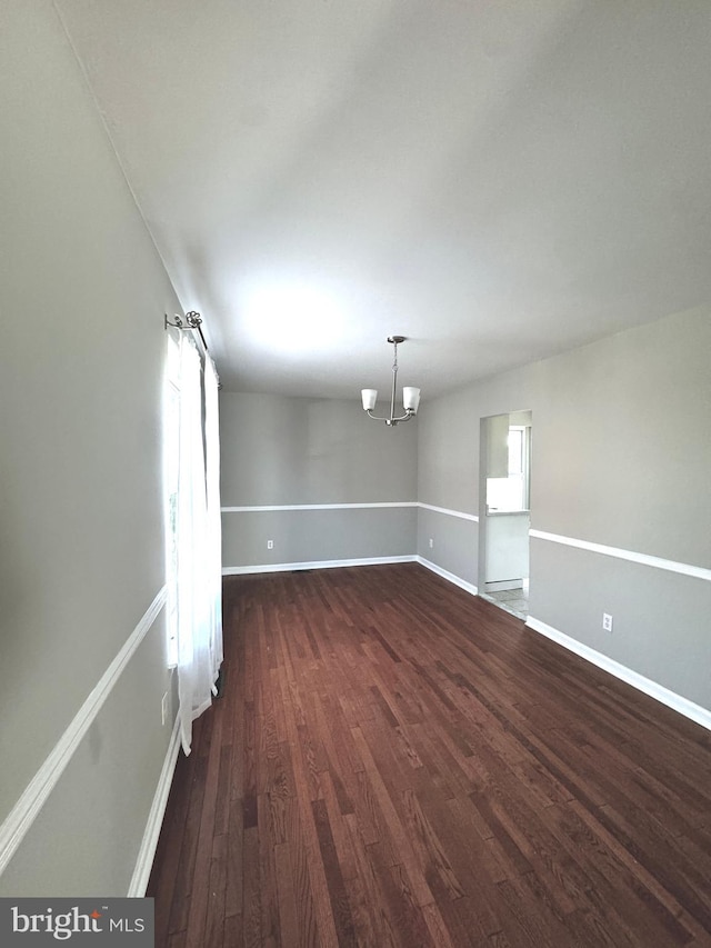 empty room with dark wood-type flooring and a notable chandelier