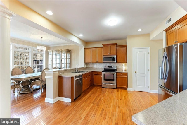 kitchen featuring sink, hanging light fixtures, light hardwood / wood-style flooring, appliances with stainless steel finishes, and kitchen peninsula