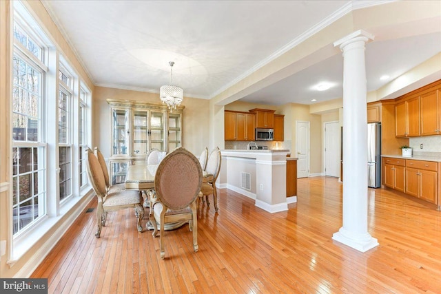 dining room with ornamental molding, light hardwood / wood-style floors, decorative columns, and a notable chandelier