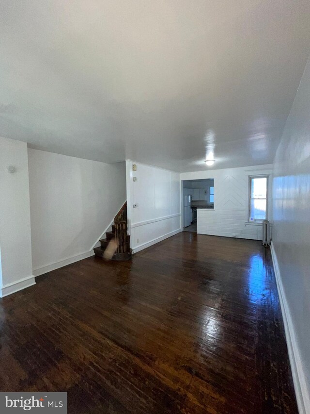 2014 Castor Ave, Philadelphia, PA 19134 - unfurnished living room featuring radiator heating unit, dark wood-type flooring, baseboards, and stairs