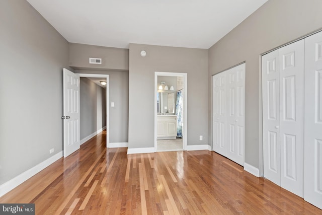 unfurnished bedroom with connected bathroom, multiple closets, and hardwood / wood-style floors