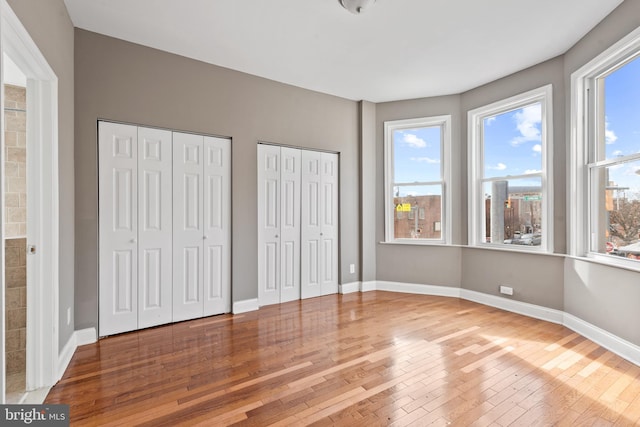 unfurnished bedroom with hardwood / wood-style floors and multiple closets