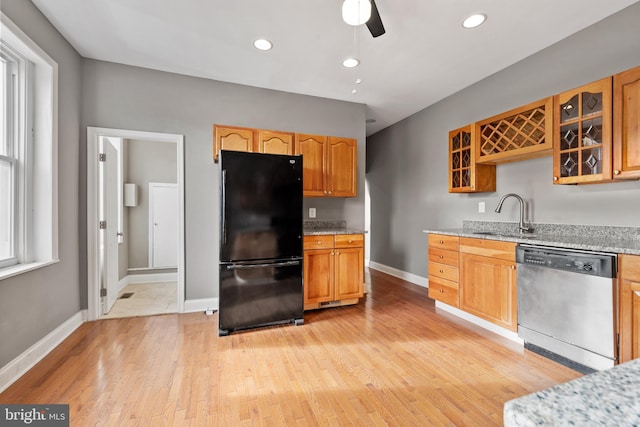 kitchen with black refrigerator, sink, stainless steel dishwasher, light stone countertops, and light hardwood / wood-style floors